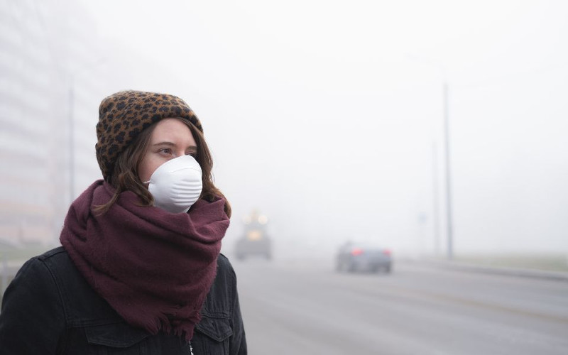 Kobieta w maseczce na tle zasmogowanego miasta